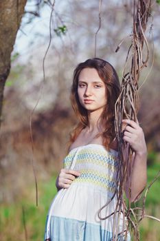 Pregnant woman in spring park. Hand holding on to a climbing plant