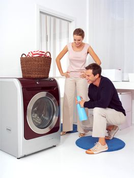 Man puts clothes into the washing machine while woman smiling