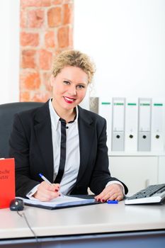 Young female lawyer working in her office with typical law book and writing document