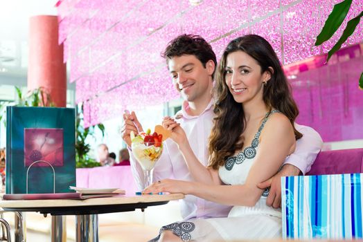 Young Couple in a Cafe eating together an ice cream sundae being happy after shopping, bags standing behind them