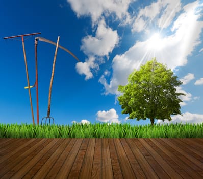 Agricultural landscape and wooden floor with grass, green tree, rake, scythe and pitchfork