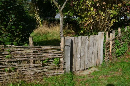 Rustic wooden garden gate with willow wood wattle fence at a rural cottage garden in Sussex,England.