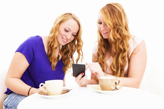 two redhead women sitting at a coffee table busy with a smartphone on white background