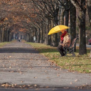 Mature woman in the fall park with yello umbrella