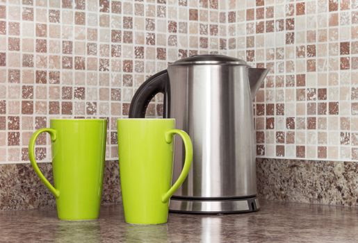 Metal electric kettle and green cups in the kitchen.