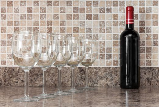 Bottle of red wine and empty glasses on kitchen countertop.