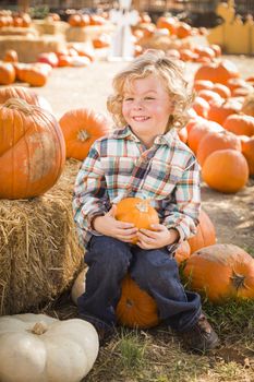 Adorable Little Boy Sitting and Holding His Pumpkin in a Rustic Ranch Setting at the Pumpkin Patch.
