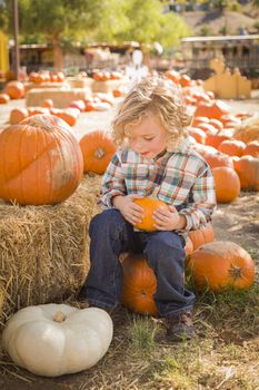 Adorable Little Boy Sitting and Holding His Pumpkin in a Rustic Ranch Setting at the Pumpkin Patch.
