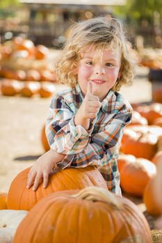 Adorable Little Boy Leaning on Pumpkin Gives a Thumbs Up in a Rustic Ranch Setting at the Pumpkin Patch.