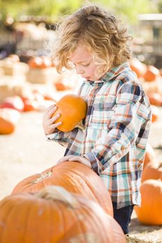 Adorable Little Boy Sitting and Holding His Pumpkin in a Rustic Ranch Setting at the Pumpkin Patch.
