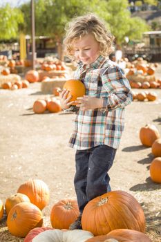 Adorable Little Boy Sitting and Holding His Pumpkin in a Rustic Ranch Setting at the Pumpkin Patch.
