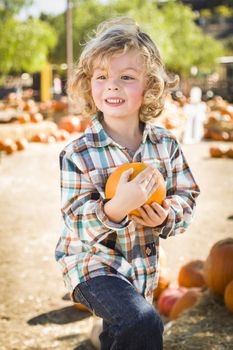 Adorable Little Boy Sitting and Holding His Pumpkin in a Rustic Ranch Setting at the Pumpkin Patch.
