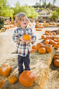 Adorable Little Boy Sitting and Holding His Pumpkin in a Rustic Ranch Setting at the Pumpkin Patch.

