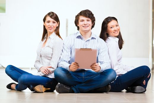 portrait of a group of young people sitting on the floor, man and two attractive women