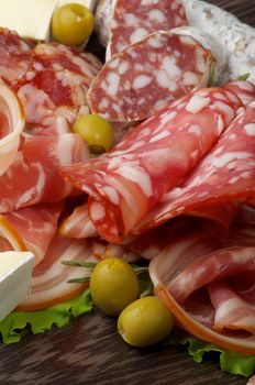 Delicatessen Cold Cuts with Smoked Ham, Pepperoni, Salami, Finocchiona, Green Olives and Camembert Cheese closeup on Dark Wooden background