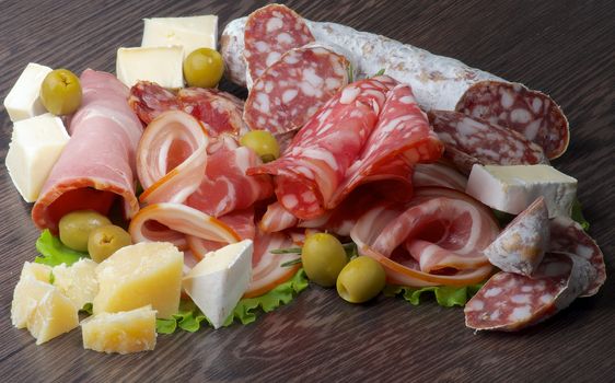 Arrangement of Delicatessen Cold Cuts with Smoked Ham, Pepperoni, Salami, Finocchiona, Green Olives, Grana Padano and Camembert Cheese closeup on Dark Wooden background