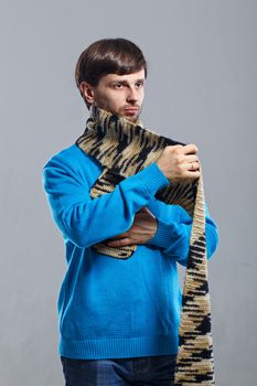 Young man in a sweater wraps a scarf around the neck