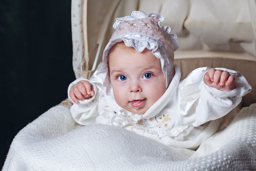 Cheerful and happy blue-eyed baby in  bonnet lies in cradle