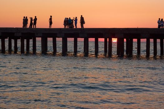 Groups of people on the old pier are photographed and admire the beautiful sunset over the Black Sea coast in Crimea, Ukraine