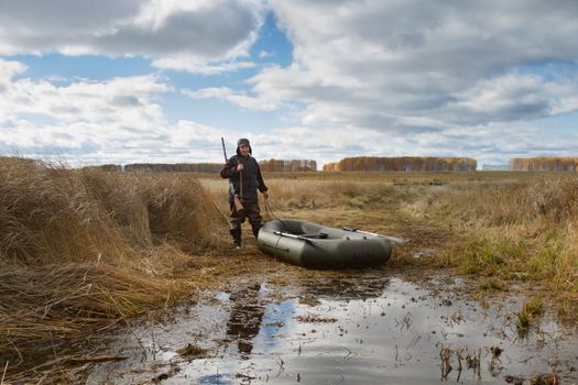 Hunter and inflatable boat on the shore of the lake overgrown with reeds