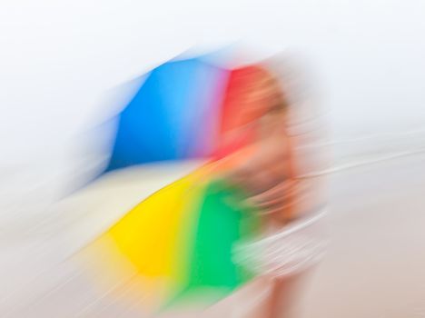 Rain and wind. Abstract image of girl with colorful umbrella against the sea.  Intentional motion blur
