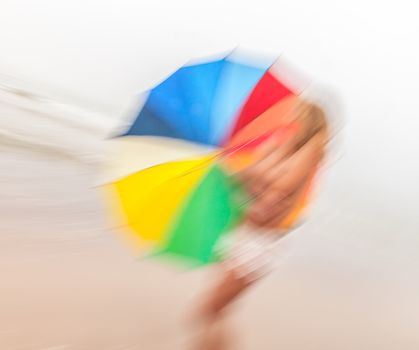 Rain and wind. Abstract image of girl with colorful umbrella against the sea.  Intentional motion blur