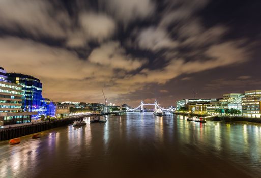 Floodlit HMS Belfast, Tower Bridge and Tower of London on River Thames with reflections in the water