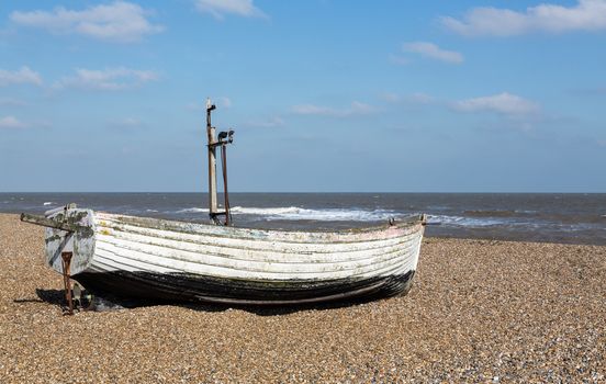 Ancient wooden painted fishing boat on pebble beach by North Sea in Aldeburgh Suffolk on East coast of England