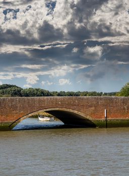 Road arch over Norfolk Broads river with small white rowing boat moored by the bank