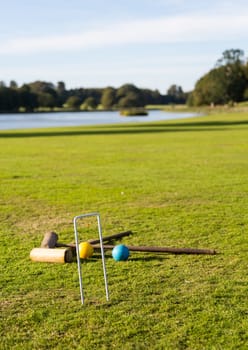 Two wooden mallets of croquet set and hoop set into green english lawn as though the game is just over