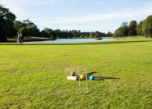Two wooden mallets of croquet set and hoop set into green english lawn as though the game is just over