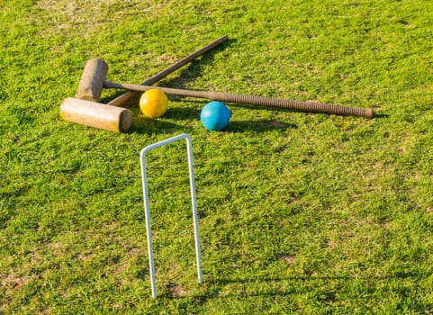 Two wooden mallets of croquet set and hoop set into green english lawn as though the game is just over
