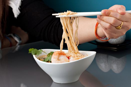Closeup of a woman eating shrimp and Thai noodles from a bowl with chopsticks.