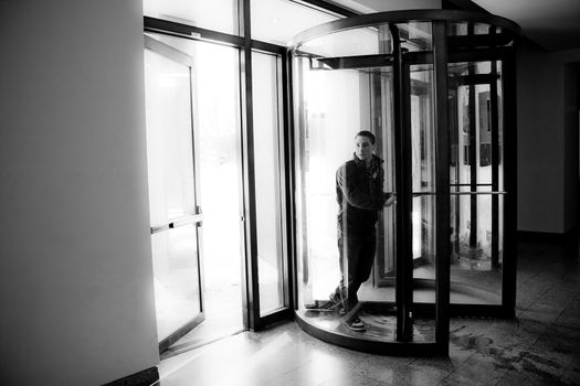 Young man in his twenties walks through a revolving doorway entrance. Black and white.