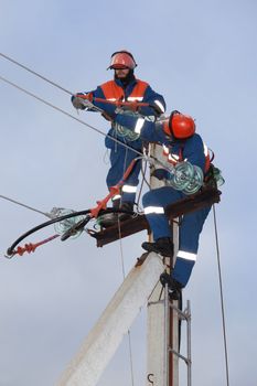 Two electrician working on top of an electricity pylon with the use of  ladder and belt