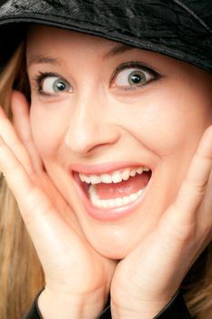 Close-up of blonde female face looking happily surprised with hands on her chin