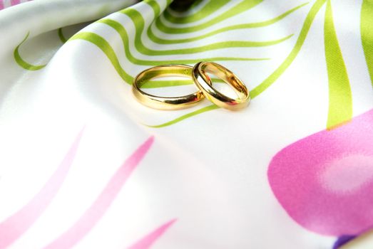 Close-up photo of two wedding rings on a colorful fabric