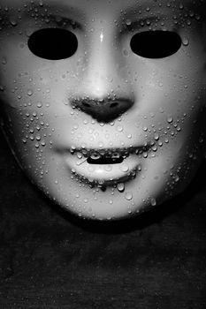 Wet plastic mask on a dark wooden background. Close-up monochrome photo