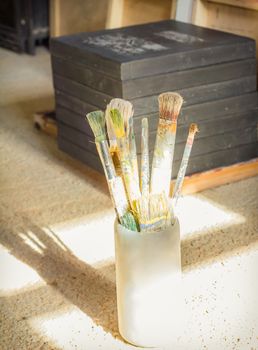 Paint brushes set on jar, in front of artistic canvas