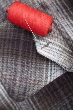 Red sewing spool with needle on a flannel fiber. Close-up photo
