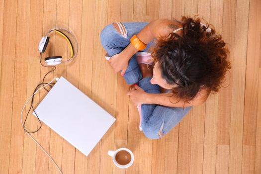 A girl sitting on the floor with a Laptop and some coffee.