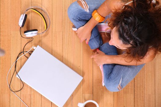 A girl sitting on the floor with a Laptop and some coffee.