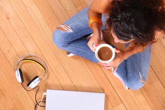 A girl sitting on the floor with a Laptop and some coffee.