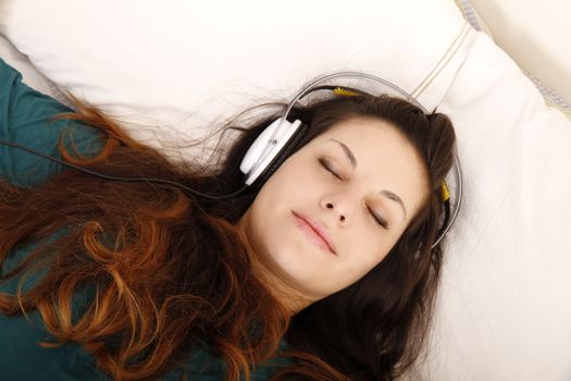 A young adult woman listening music with headphones in bed.