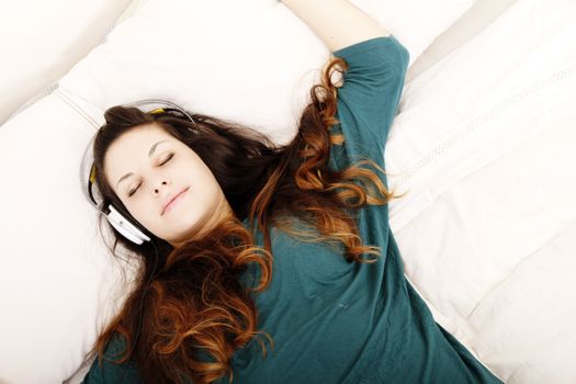 A young adult woman listening music with headphones in bed.