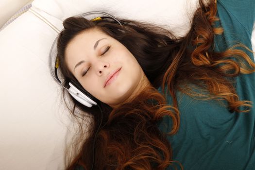 A young adult woman listening music with headphones in bed.