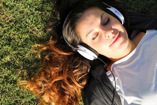 A young woman enjoying the sunlight in the Park an listening music			
