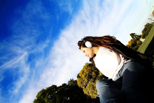 A young woman enjoying Music and sitting on the pavement.