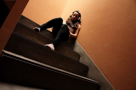 A young woman listening to melancholic Music sitting in the stairway.