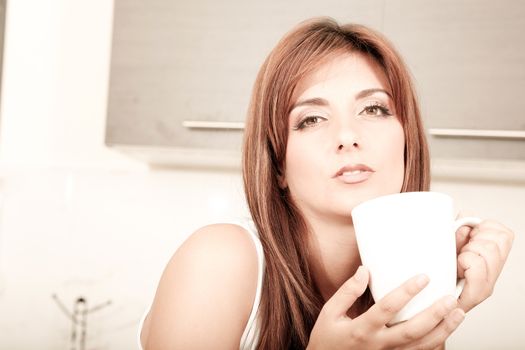 A young adult woman sitting in the kitchen with a cup of coffee. 